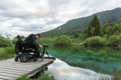 Persona en silla de ruedas junto a un lago, sobre una pasarela