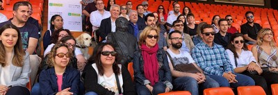 El grupo al completo posa, en la tribuna de Mestalla, sentados en torno a la escultura conmemorativa del afiliado y vendedor de la ONCE Vicente Navarro