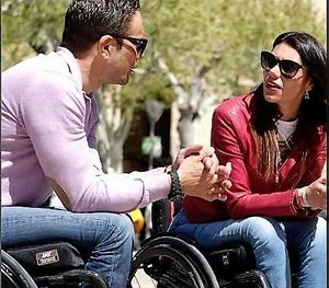 Dos jóvenes (un chico y una chica) charlan desde sus respectivas sillas de ruedas en un parque urbano