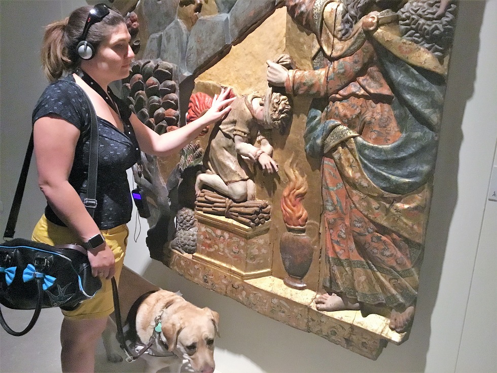 Una afiliada, acompañada de su perro guía, conoce al tacto un altorrelieve expuesto en Lerma