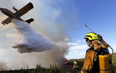 Un bombero observa un incendio forestal mientras un hidroavión descarga agua sobre las llamas