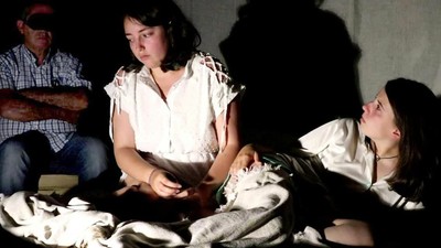 Momento del montaje "Coa mirada nas súas mans" con actrices en primer plano y espectador al fondo con antifaz