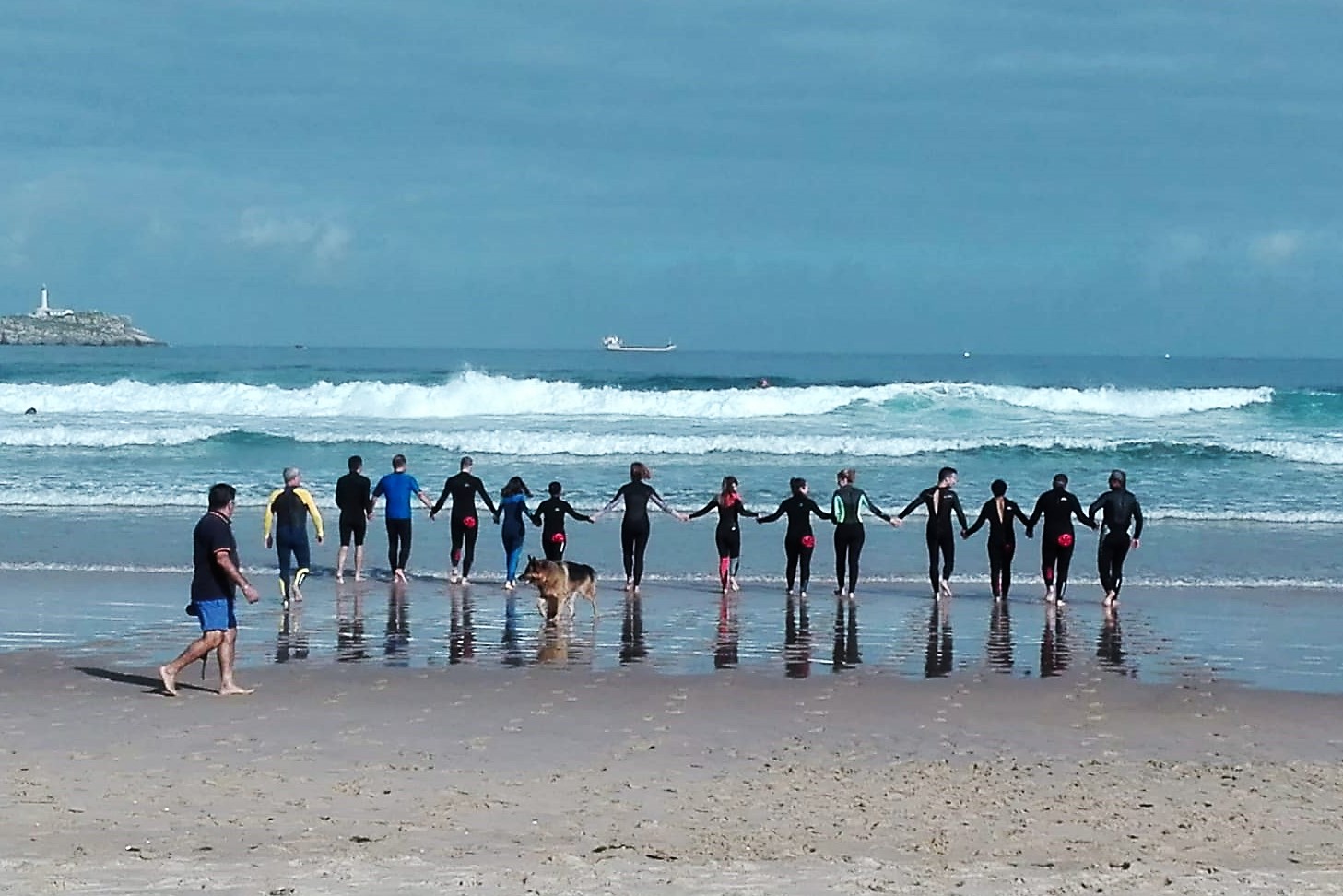 El grupo, aún unido por las manos, reconociendo el oleaje a pie de playa