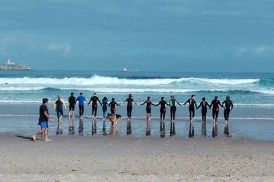 El grupo, aún unido por las manos, reconociendo el oleaje a pie de playa
