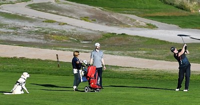 Un joven ciego, con su perro guía al lado, escucha las instrucciones de golpeo que le imparte el profesor en el campo de golf