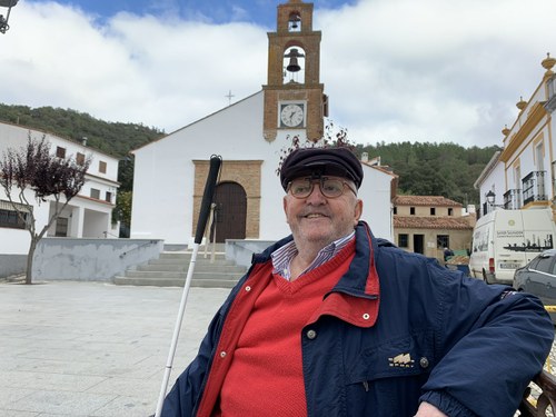 El protagonista posa sentado en un banco de la plaza de la Iglesia en su pueblo de Los Romeros