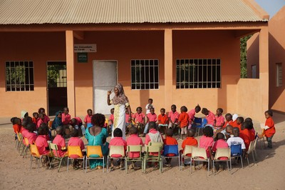 Una maestra da su lección a la clase reunida y sentada en el patio de acceso a la escuela