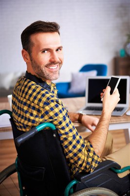 Una persona con discapacidad (en silla de ruedas) teletrabajando con su ordenador y su teléfono móvil
