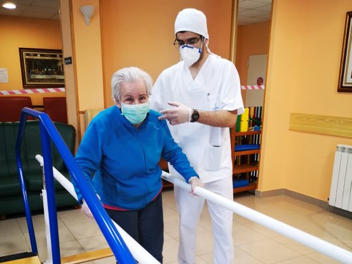 Una mujer mayor, residente, y un instructor (ambos provistos de mascarilla), en una sesión de rehabilitación en un centro de Ilunion