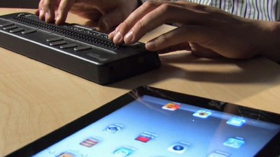 Una persona ciega maneja una tablet a través de un dispositivo de línea braille