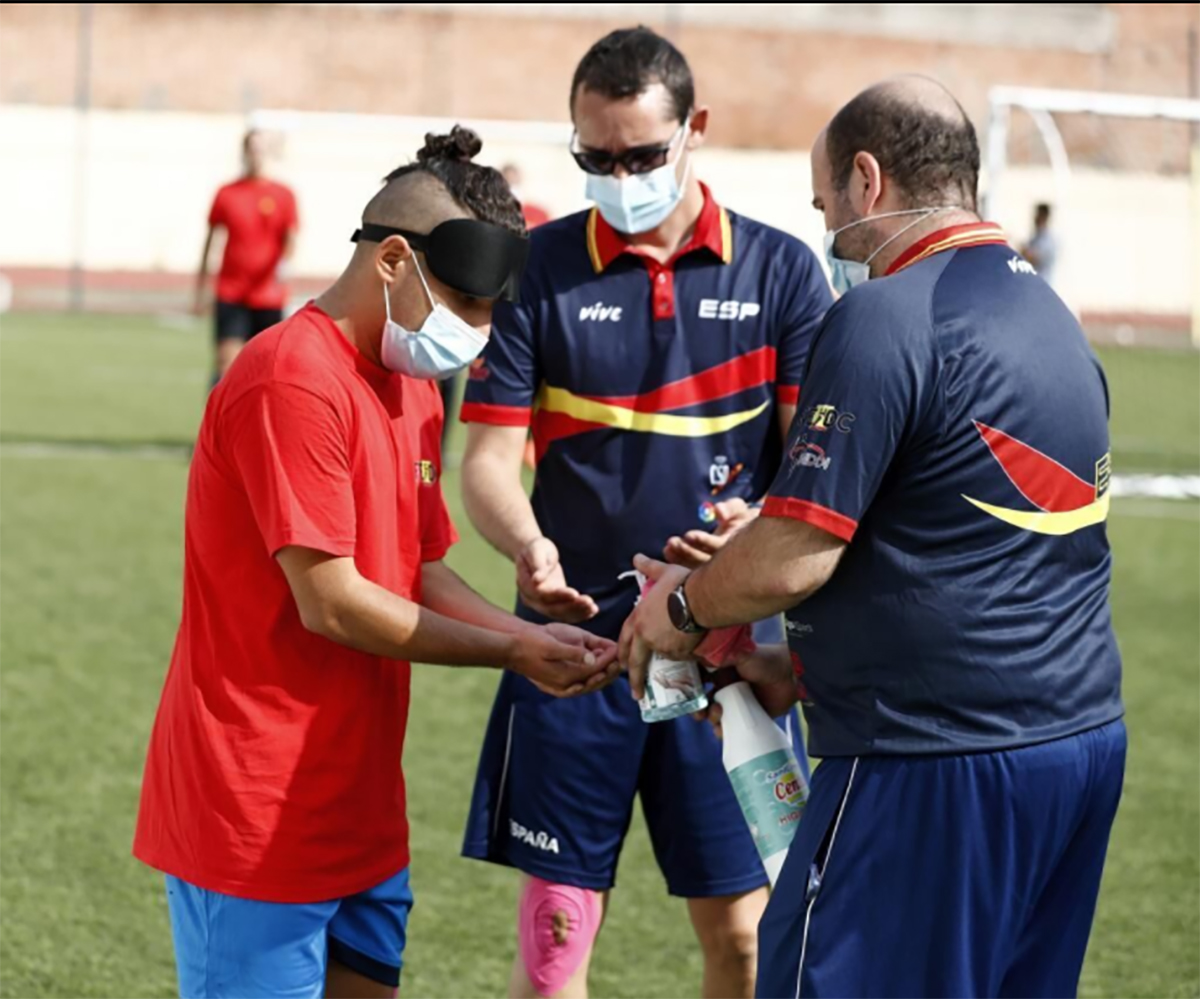 Los técnicos ayudan a uno de los jugadores a desinfectar sus manos con gel hidro-alcohólico