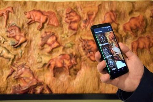 Una persona recibe en su teléfono móvil información de la aplicación Amuse sobre una exposición de reproducciones de la cueva de Altamira