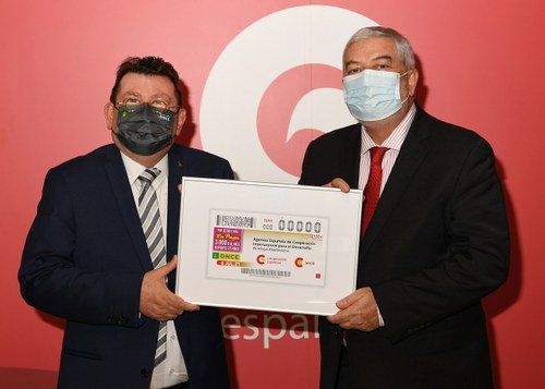 El director general de la ONCE y el de la AECID muestran el cupón enmarcado dedicado a la AECID