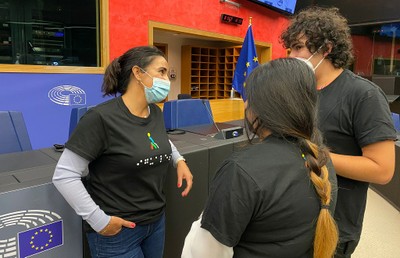 Un par de jóvenes hablan en el hemiciclo del PE con la eurodiputada Mónica Silvana, que lleva una camiseta con los puntos en braille y el isotipo del ONCELIO a color del Grupo Social ONCE