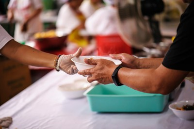 Primer plano de unas manos de un voluntario ofreciendo un plato de comida