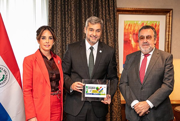 La primera dama, el presidente de Paraguay y Miguel  Carballeda muestran un cupón dedicado al país latinoamericano