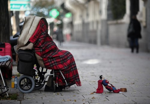 Persona en silla de ruedas tapada con una manta pidiendo en una calle de Madrid