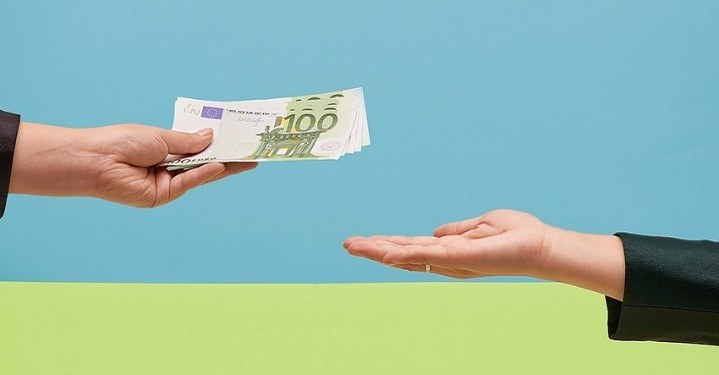 Una mano entregando billetes de 100 euros a otra mano