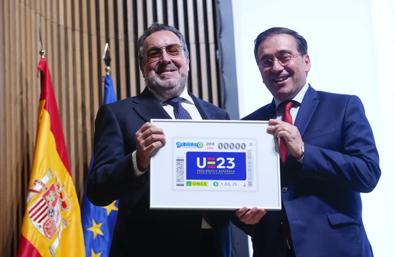Miguel Carballeda y José Manuel Albares sostienen una lámina enmarcada con el cupón