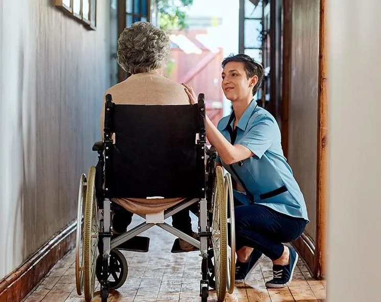 Persona mayor en silla de ruedas junto a su cuidadora