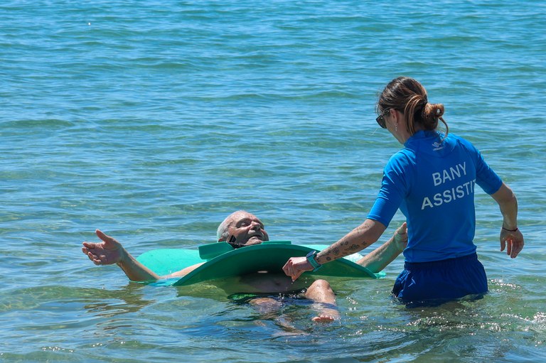 Una persona con discapacidad  bañándose en el mar con el apoyo de una asistente de Ilunion