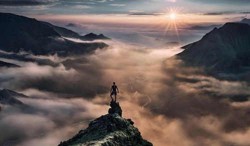 Un hombre subido en una cima alcanzando el cielo