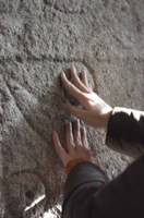 Detalle de una persona reconociendo al tacto un grabado natural en piedra en un muro de la "Ruta del Mejillón" de Arousa 
