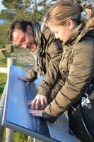 Una mujer ciega, ayudada por su acompañante, reconoce la reproducción en relieve de un perfil costero en un panel turístico de Arousa
