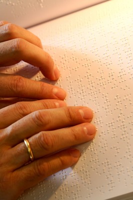 Detalle de unos dedos mientras leen un texto en braille sobre una página transcrita
