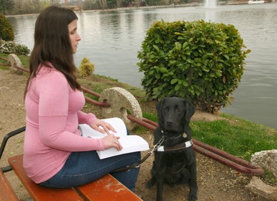 Afiliada sentada junto a su perro guía leyendo en braille