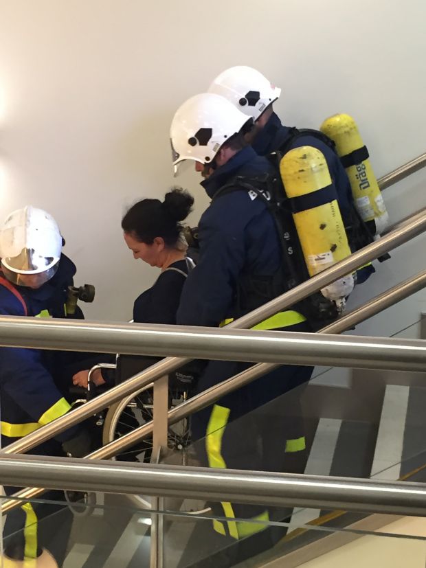 Personal de Emergencias, Fuego y Conducción de ILUNION Seguridad baja por una escalera a una persona en silla de ruedas