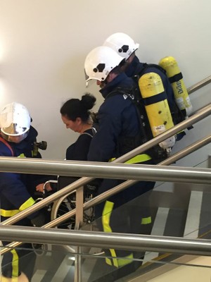 Personal de Emergencias, Fuego y Conducción de ILUNION Seguridad baja por una escalera a una persona en silla de ruedas