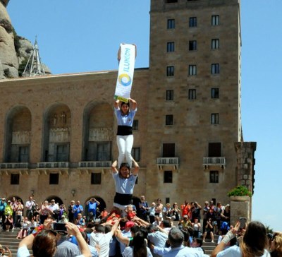 Un grupo de castellers elevan una pancarta con el nombre de Ilunion en la plaza central de la abadía de Montserrat