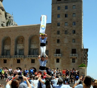 Un grupo de castellers elevan una pancarta con el nombre de Ilunion en la plaza central de la abadía de Montserrat