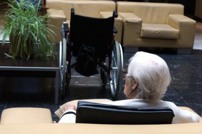 Una anciana, junto a su silla de ruedas, descansa en un sofá de una residencia de mayores