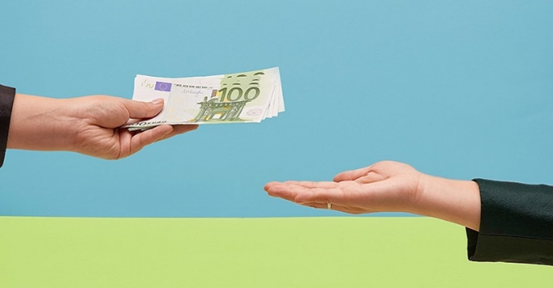 una mano entregando billetes de 100 euros a otra mano