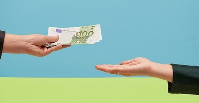 una mano entregando billetes de 100 euros a otra mano